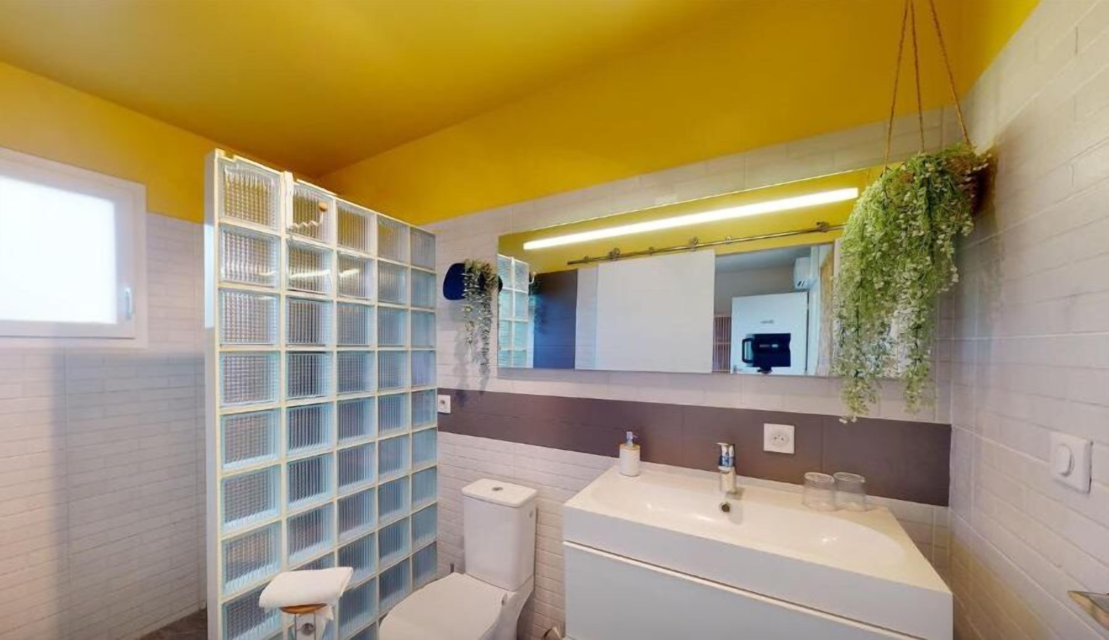 Un baño moderno con un lavamanos blanco, un inodoro y una estantería de vidrio.