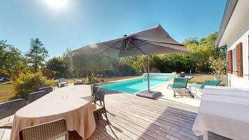 Une terrasse extérieure avec une piscine, entourée de verdure et aménagée avec des tables et des chaises.