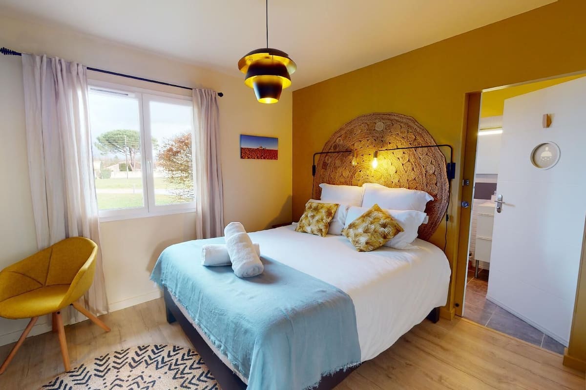 A hotel room with a bed, a chair, a window with curtains, and a door.