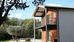 Ein modernes, zweistöckiges Haus mit Balkon, umgeben von einem gepflegten Rasen und Bäumen.