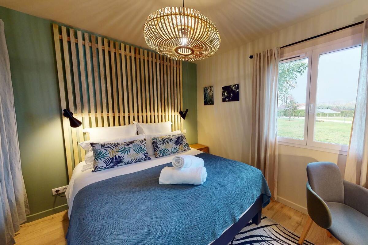 A bedroom with a bed, a chair, a window, and a hanging light fixture.