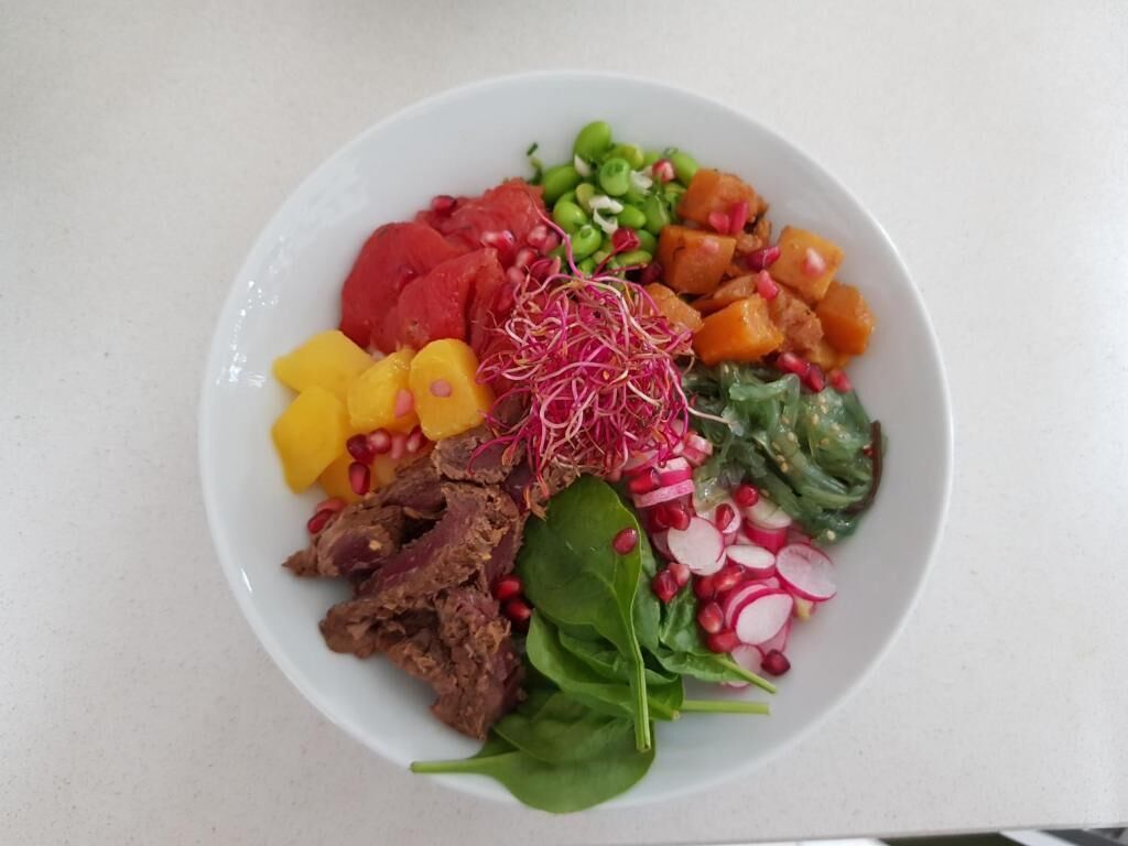 Une assiette blanche contenant divers aliments, notamment de la viande, des légumes et des germes.