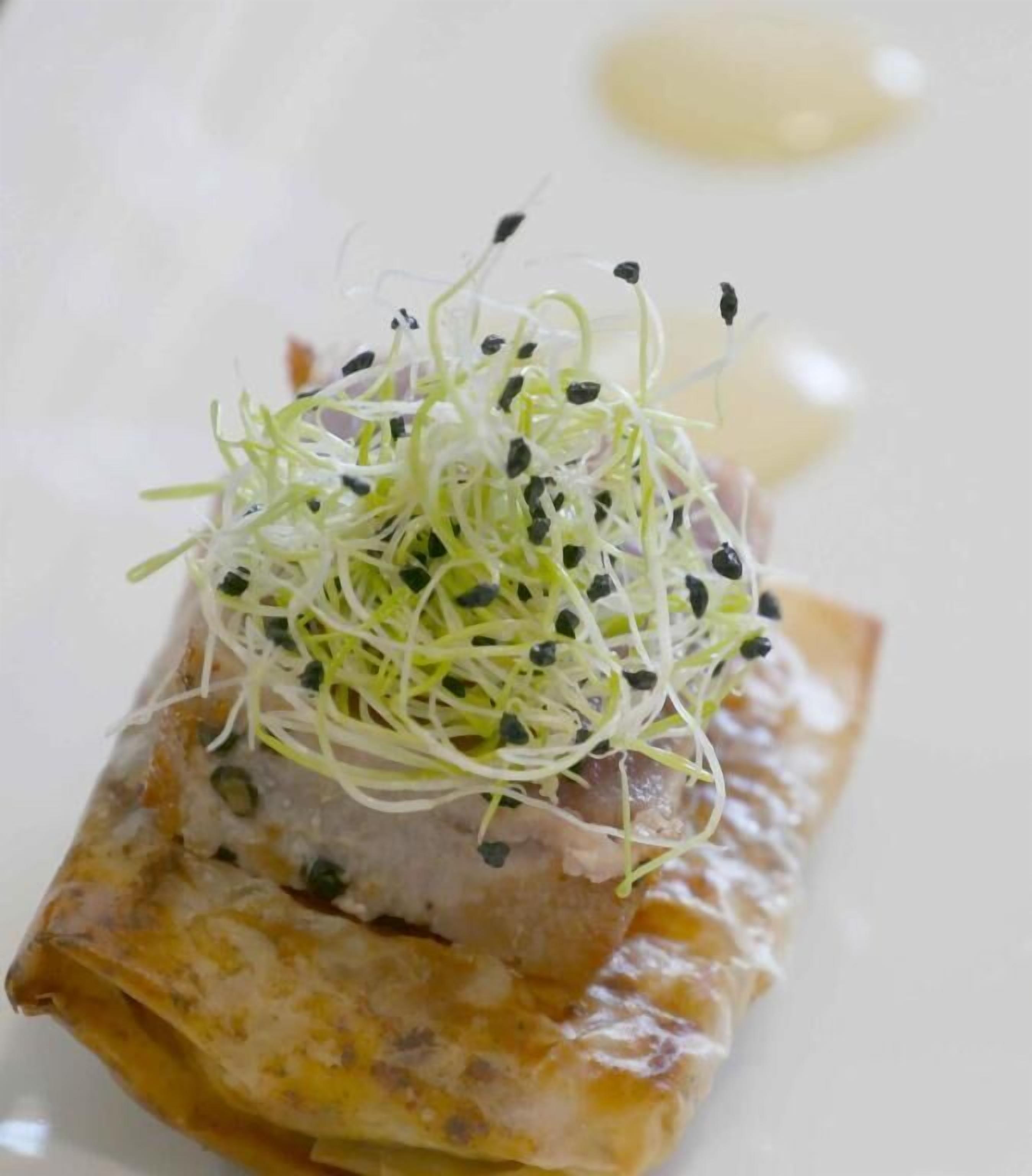 Un plat nappé d’une sauce crémeuse et agrémenté de jeunes pousses, le tout présenté dans une assiette blanche.