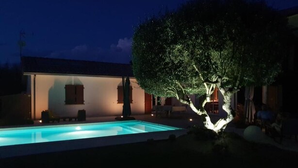 Ein Schwimmbecken mit Baum im Vordergrund, ein Gebäude mit flachem Dach und einem klaren Himmel.