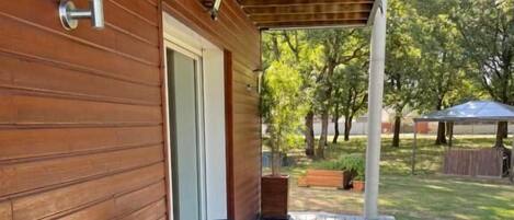 A wooden deck with a table and chairs, a door, and a covered area with trees in the background.
