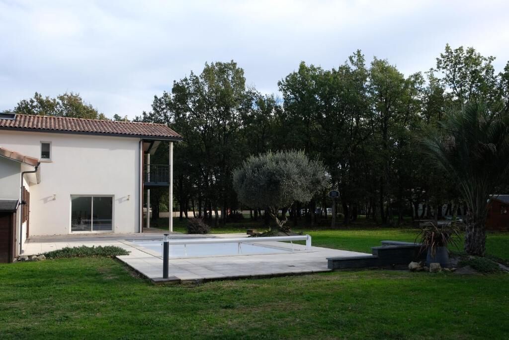 A modern two-story house with a flat roof, a patio area, and a well-maintained lawn.