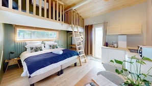 Ein Schlafzimmer mit Erkerbett, einem Bett mit blauer und weißer Bettdecke, einer Holzleiter, einem kleinen Schreibtisch mit Wasserkocher und einem Blumentopf.