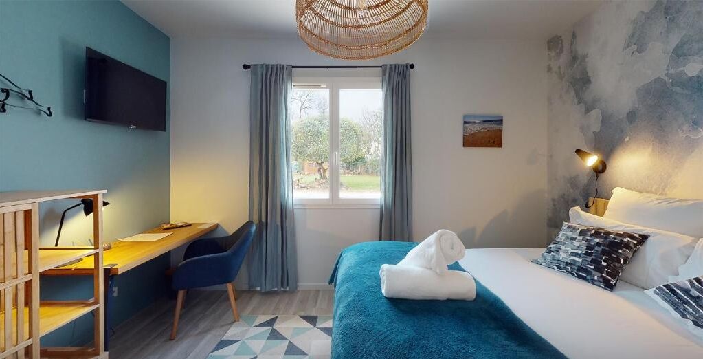 A bedroom with a bed, a desk, a chair, a television, and a window with curtains.