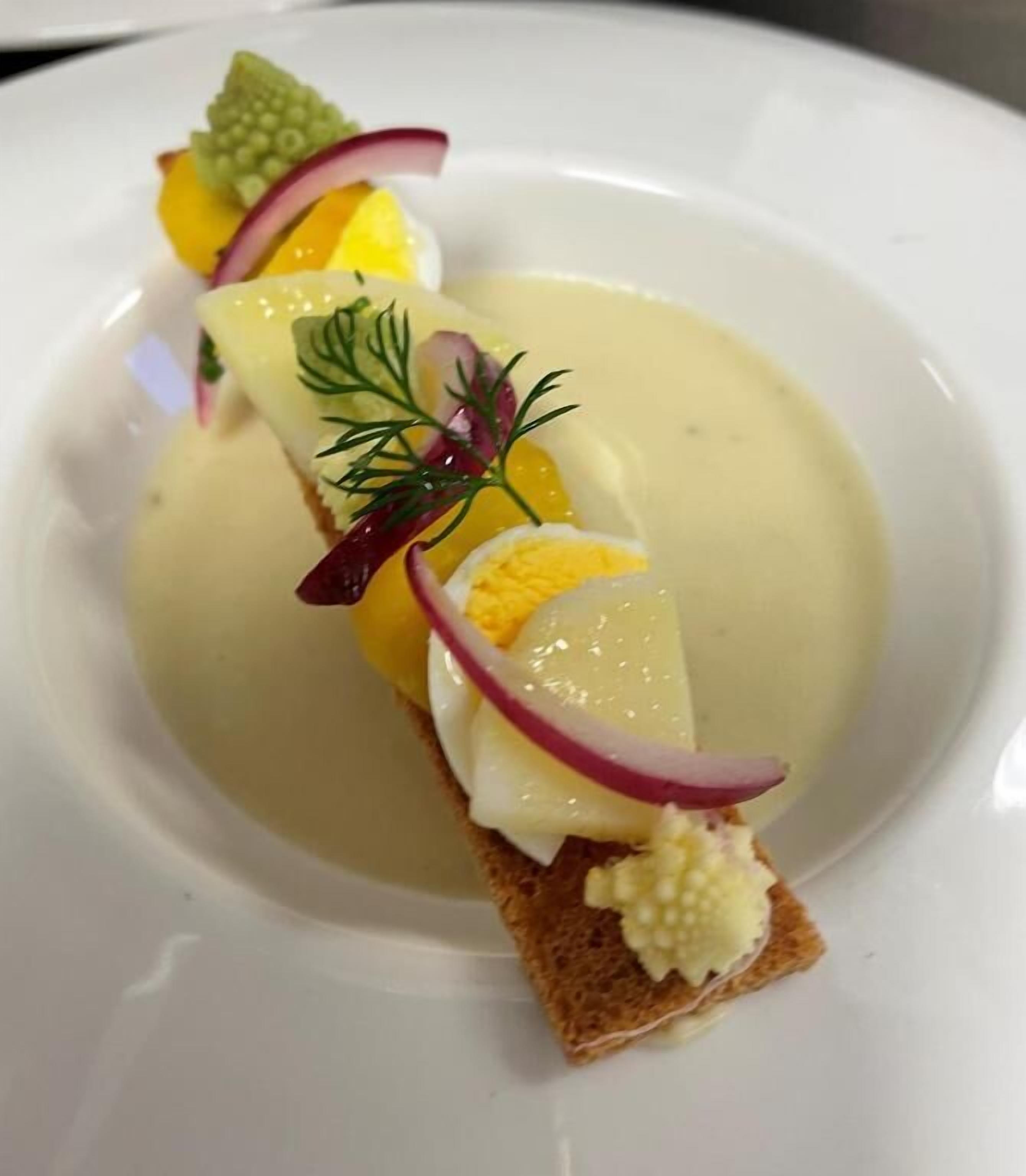 A dish with a slice of bread topped with a creamy sauce, a boiled egg, and garnishes of dill and radish.