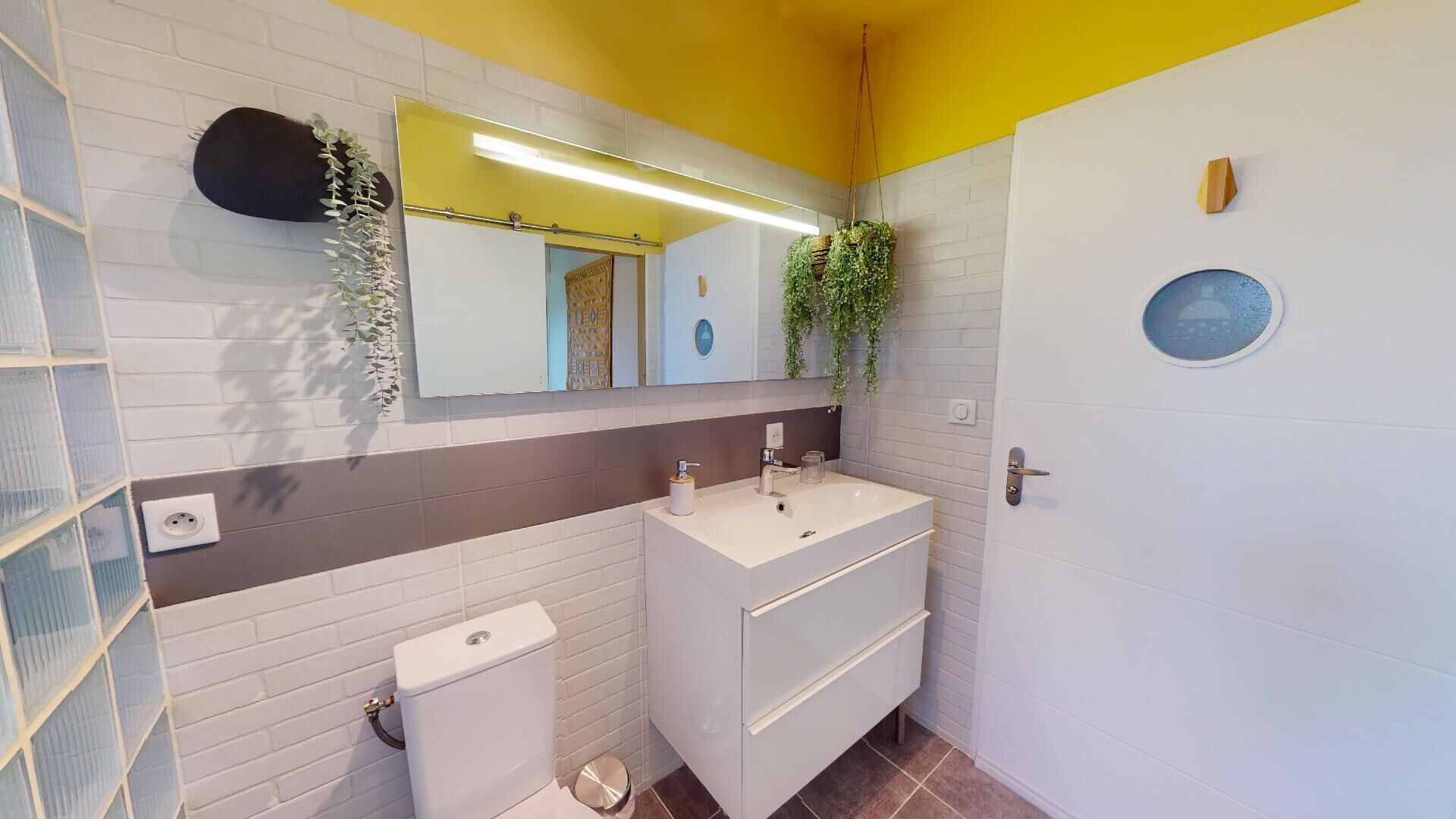 A bathroom with a white sink, a toilet, a mirror, and a door with a round window.