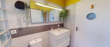 A bathroom with a white sink, a toilet, a mirror, and a door with a round window.