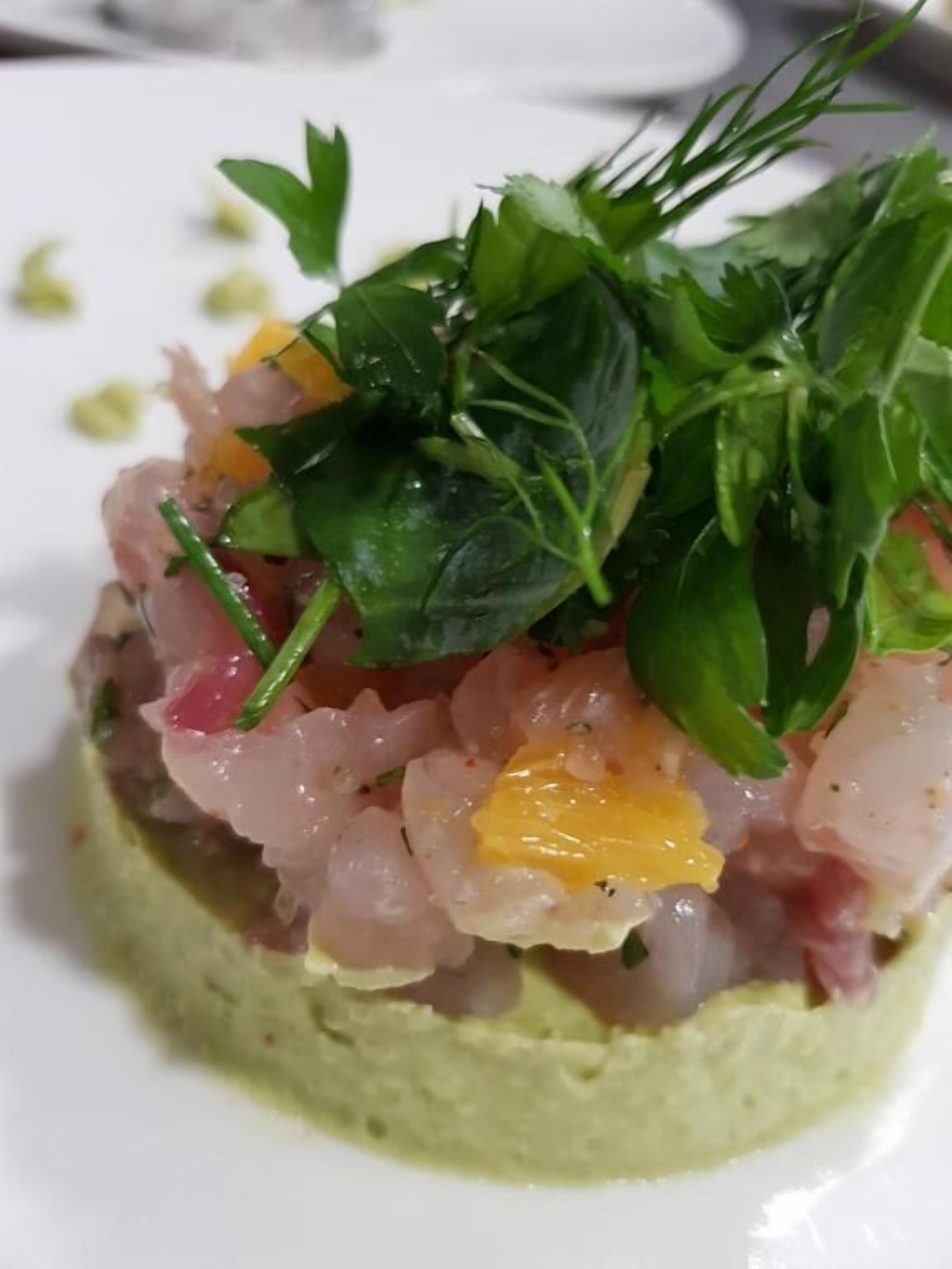A dish with a green base, possibly a puree, topped with pinkish ingredients and green leaves.