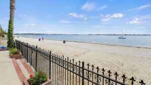 A beach with a metal fence, a palm tree, and a boat on the water. - Condo on the Bay! Prime Location!  (San Diego)