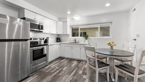 A modern kitchen with stainless steel appliances, white cabinetry, and a dining area with a round table and chairs. - Condo on the Bay! Prime Location!  (San Diego)