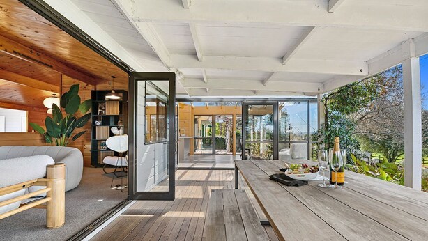 Un intérieur moderne avec un plancher en bois, un canapé, une table à manger avec de la nourriture et des boissons, et une vue sur l’extérieur.