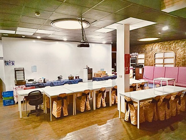 A conference room with multiple tables and chairs, a kitchenette, and a seating area with a pink couch.