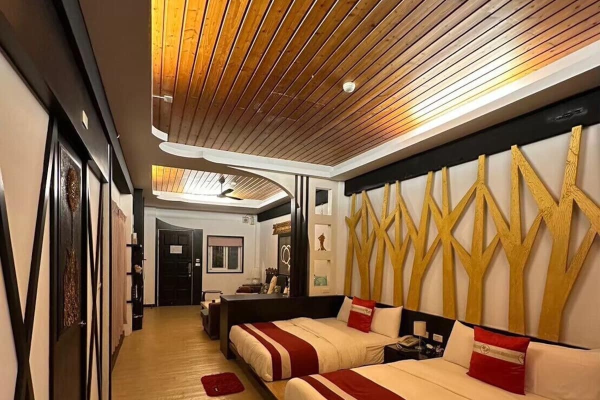 A hotel room with a wooden ceiling, a large bed with red and white bedding, a desk, and a mirror.