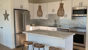Uma cozinha moderna com armários brancos, geladeira de aço inoxidável, microondas e uma ilha grande com banquetas.