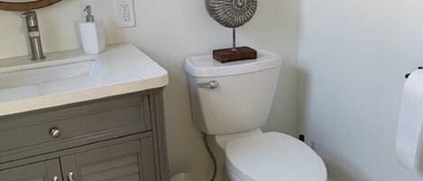 A bathroom with a white toilet, a grey cabinet, a round mirror, a starfish decoration, and a pebble-patterned floor.