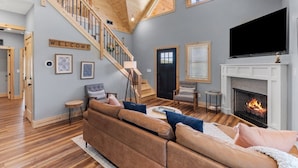 Amplia sala de estar con escalera de madera, chimenea y televisor.