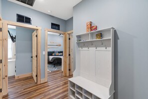 A room with a wooden floor, a white wardrobe with hooks, and a bed with a colorful blanket.
