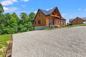 A wooden cabin with a sloped roof, a porch, and a gravel driveway.