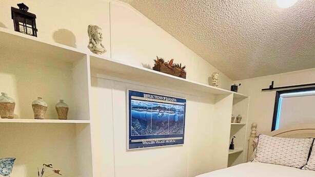 Une chambre à coucher avec un lit, une étagère ornée d’objets décoratifs, un tableau encadré et un plancher en bois.
