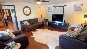 Un salon avec un canapé en cuir, un téléviseur, un ventilateur de plafond et un grand tapis blanc.