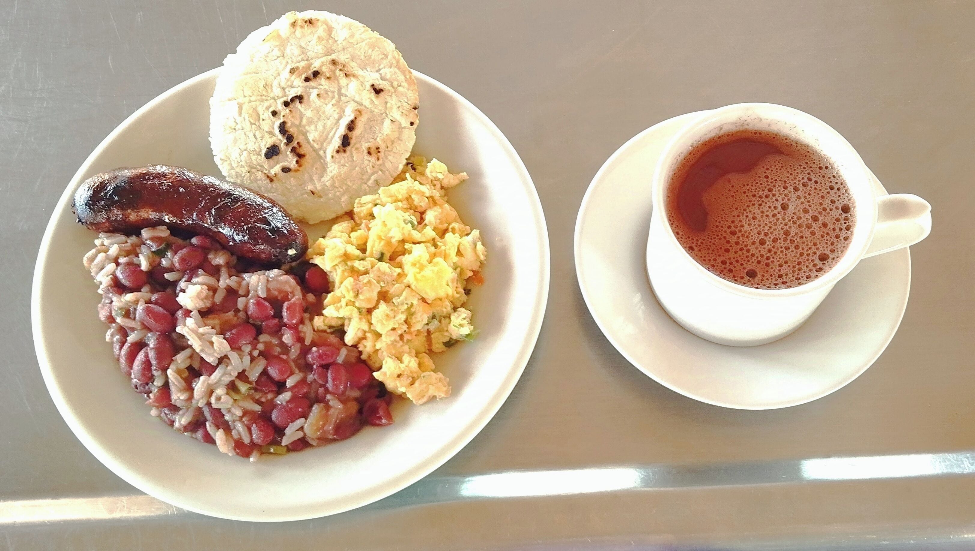 A plate of food including beans, scrambled eggs, and a sausage, alongside a cup of coffee on a table.