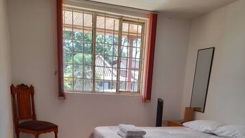Un dormitorio con cama, una silla, una mesita de noche y una ventana con cortinas.