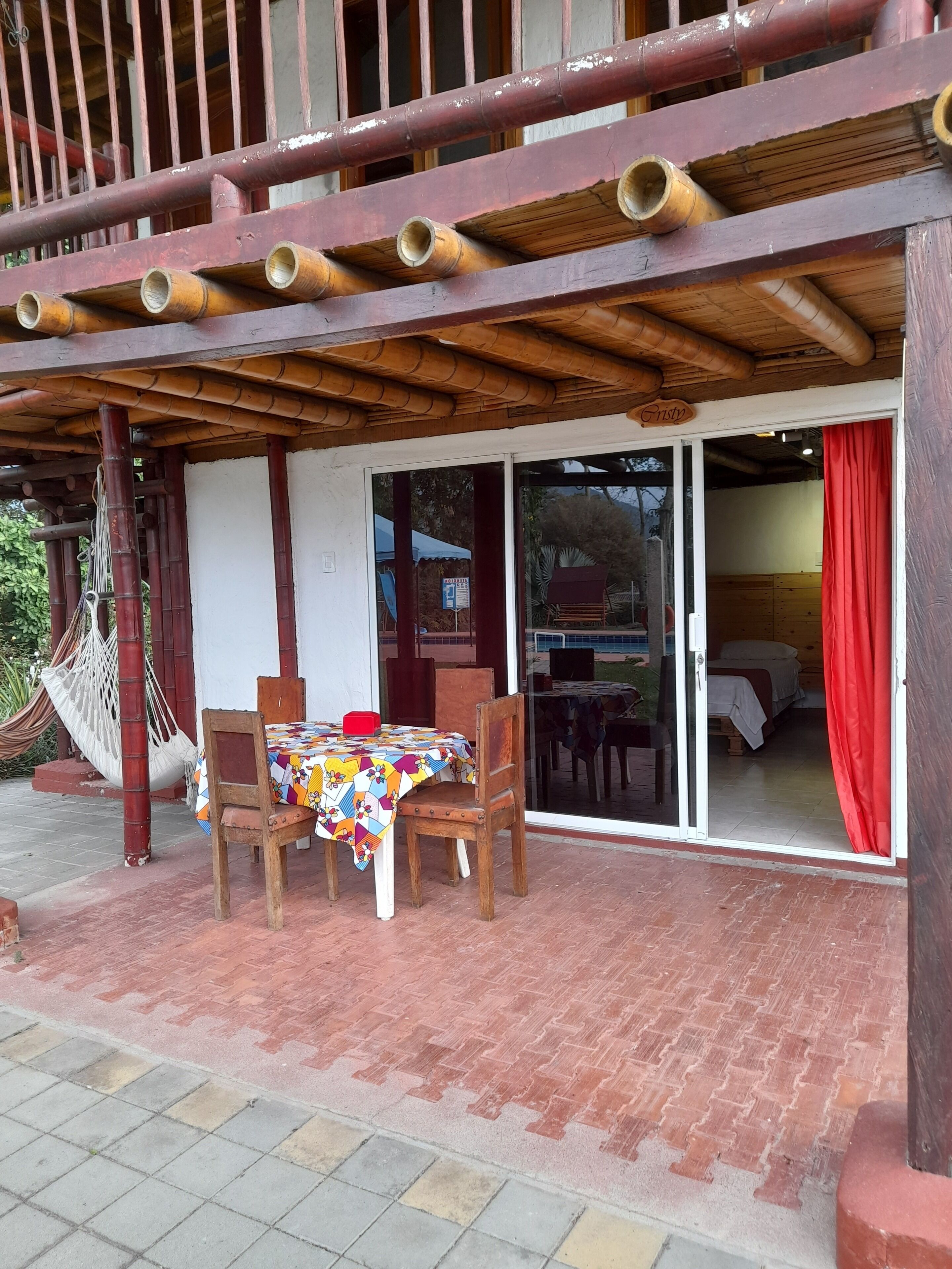 A covered outdoor seating area with a table and chairs, a hammock, and a sliding glass door leading to an interior space.