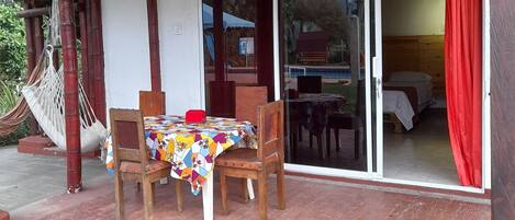 A covered outdoor seating area with a table and chairs, a hammock, and a sliding glass door leading to an interior space.