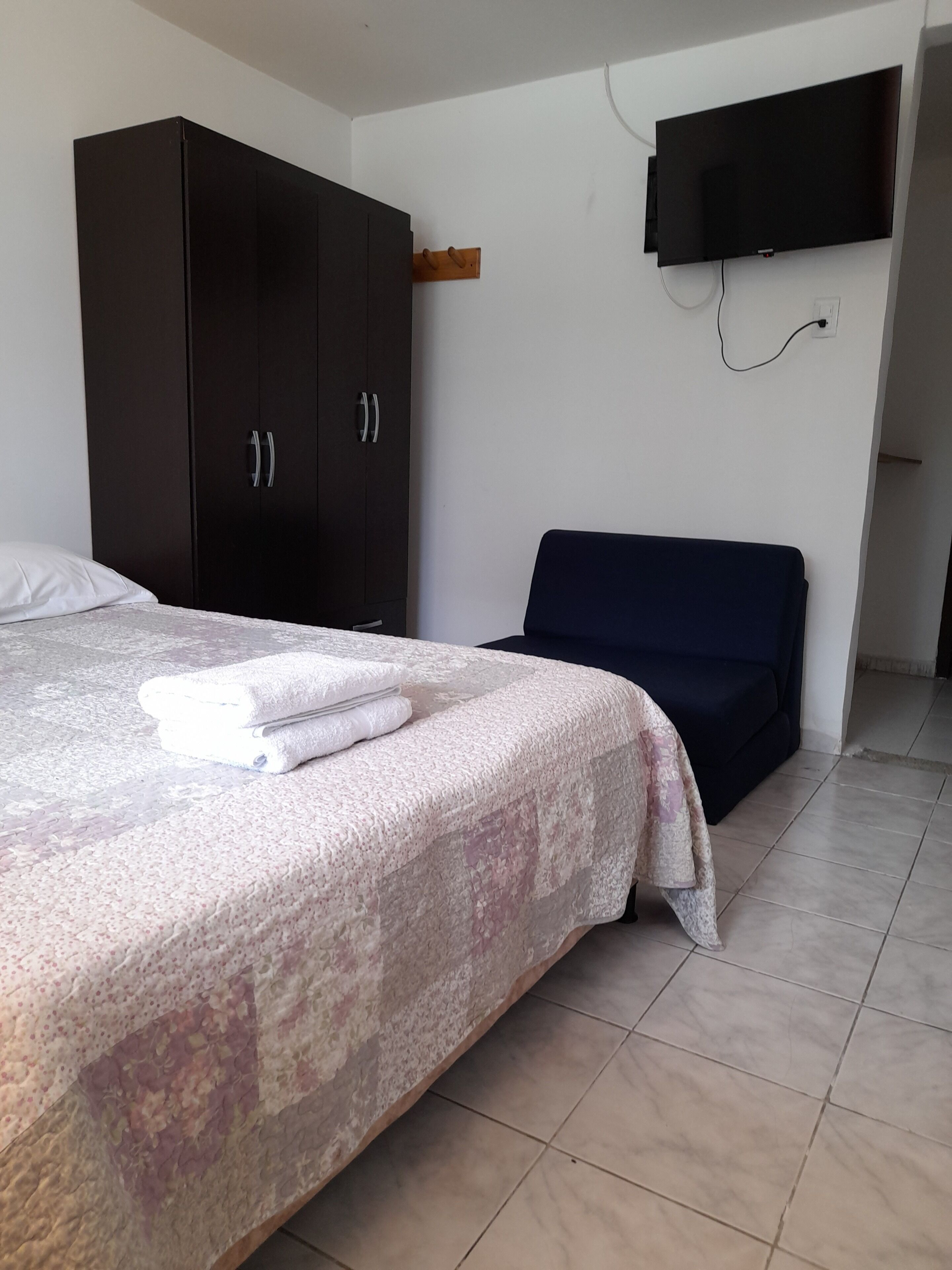 Un dormitorio con cama, un armario oscuro, un televisor de pantalla plana montado en la pared y un sofá azul.