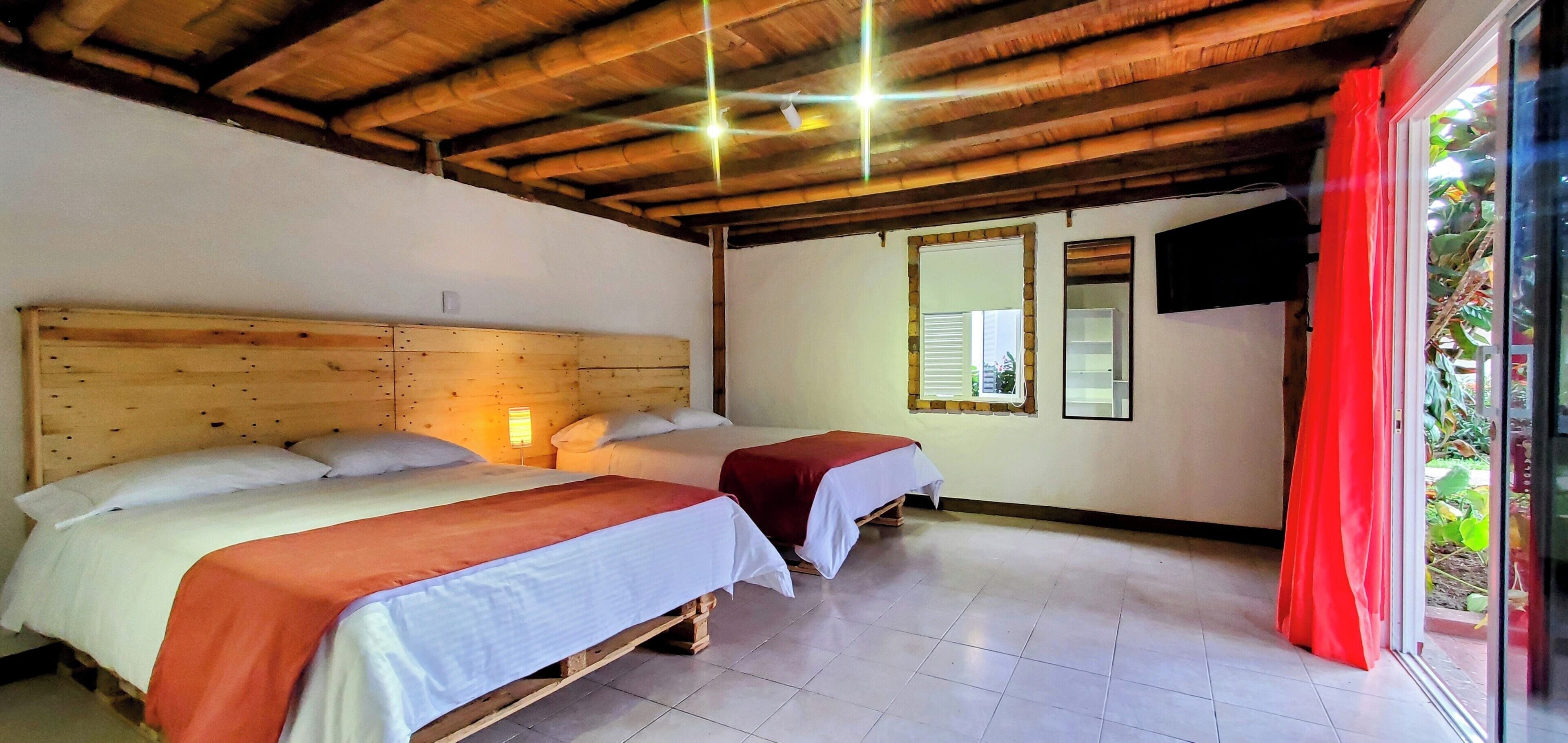 Una habitación con dos camas, cabeceros de madera, piso de baldosas, una ventana con contraventanas y un televisor fijado a la pared.
