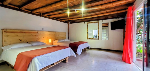 A room with two beds, wooden headboards, a tiled floor, a window with shutters, and a television mounted on the wall.