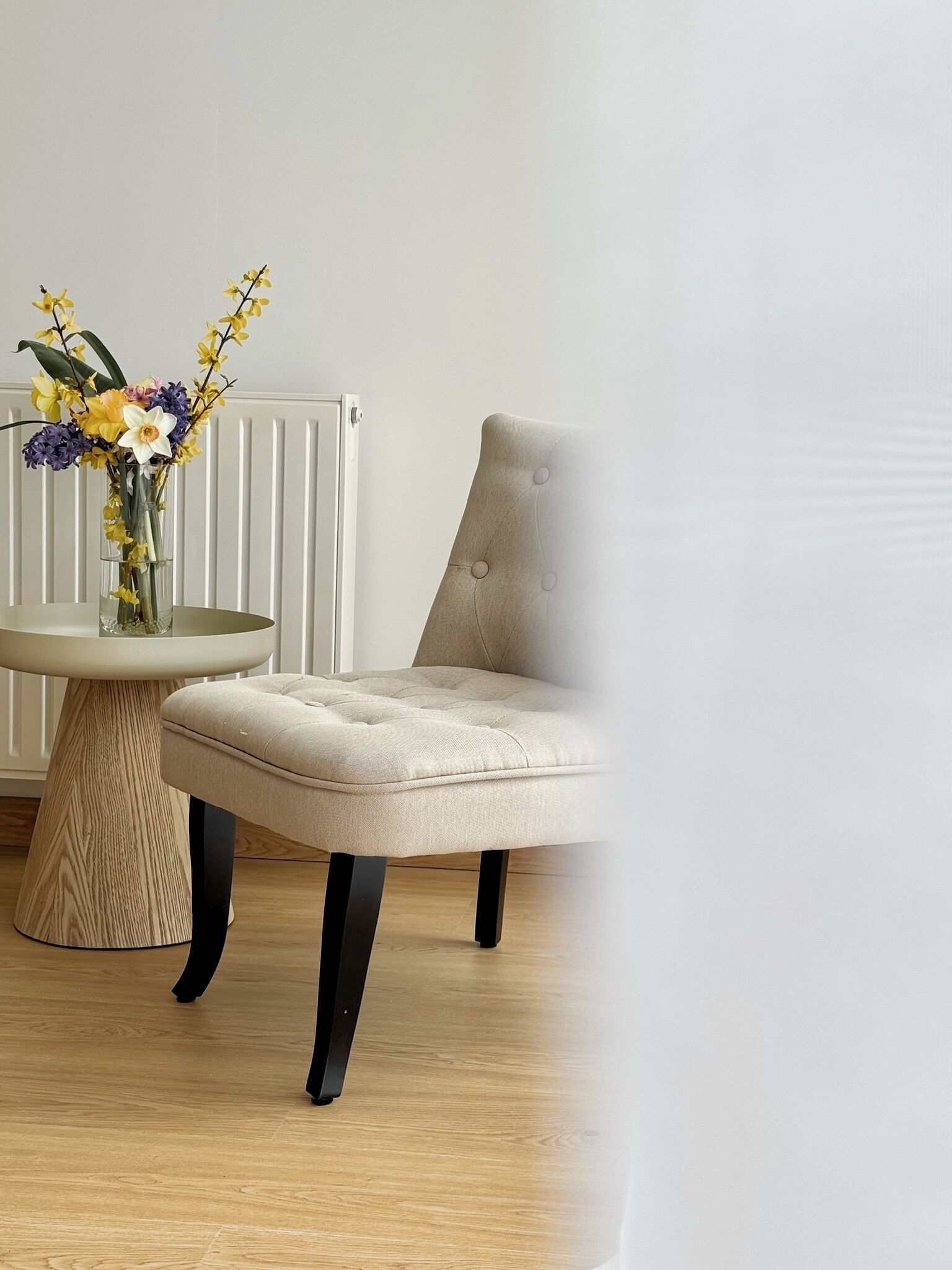 Et værelse med et rundt bord, en beige polstret stol og en vase med blomster.