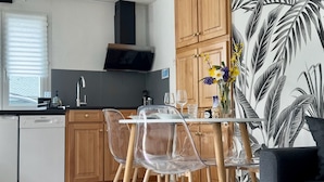 A modern kitchen with wooden cabinets, a built-in oven, and a dining area with clear chairs and a table. - Studio Cosy (Mende)