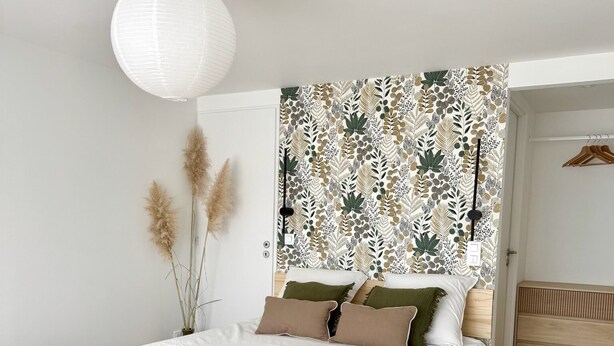 A bedroom with a bed, bedside table, and a wall with a leaf pattern. - Studio Cosy (Mende)