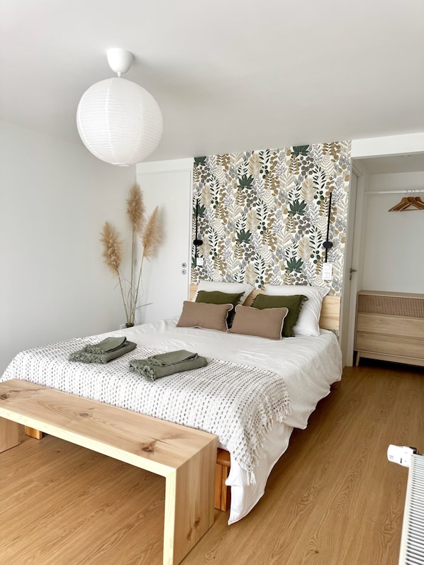 Ein Schlafzimmer mit Bett, Nachttisch und einer Wand mit Blätermotiv.