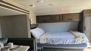 Ein kompaktes Wohnmobil-Interieur mit Bett, Sitzgruppe und kleiner Küchenzeile.