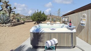 Ein Whirlpool mit Handtuch und Flasche, umgeben von Wüstenpflanzen und einem Holzzaun.