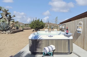Relax in the backyard hot tub surrounded by lush greenery and a serene hillside view.