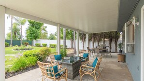 Portico coperto con mobili in vimini e un tavolo con piano in vetro, immerso in un giardino e con vista sul retrostante.