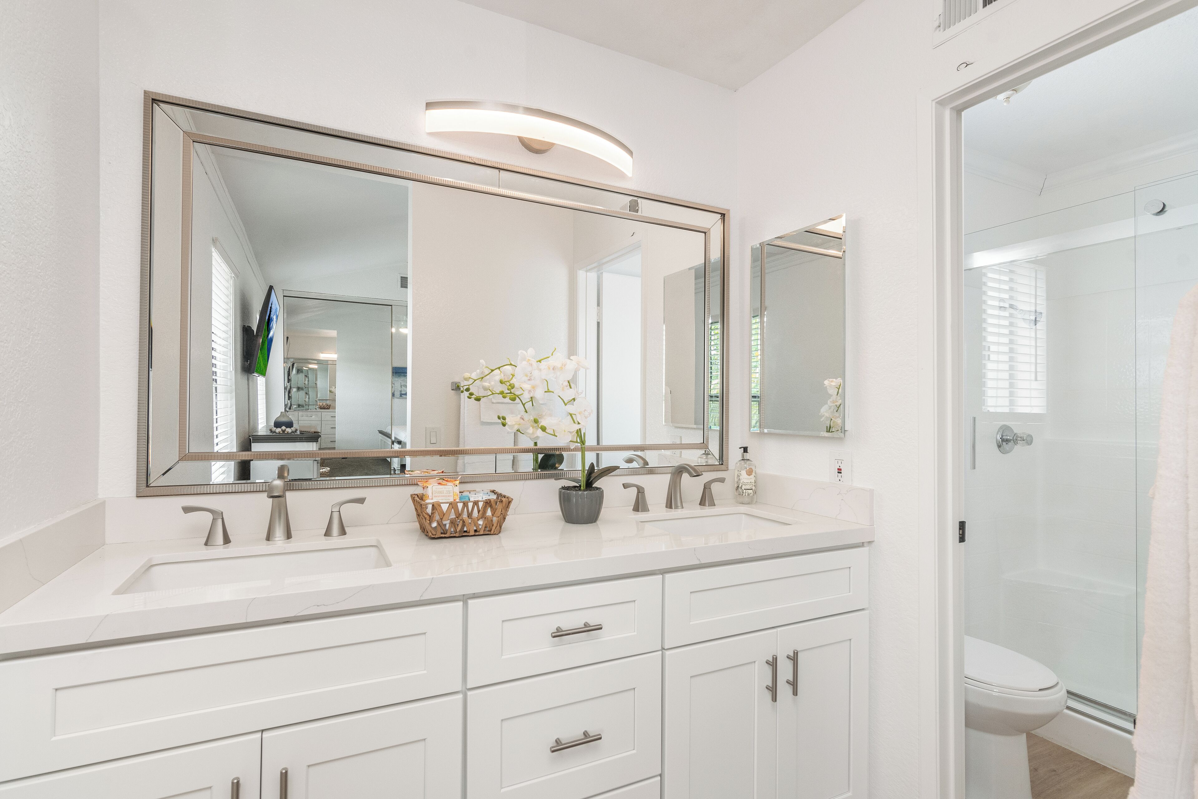 A modern bathroom with two sinks, a large mirror, and a shower.