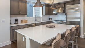 A modern kitchen with dark wood cabinets, stainless steel appliances, and a large island with bar stools. - Luxury Townhome in the Heart of Big Sky (Big Sky)