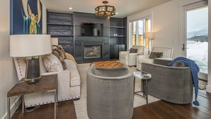 A modern living room with a fireplace, comfortable seating, and a view of the outdoors. - Luxury Townhome in the Heart of Big Sky (Big Sky)