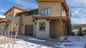 A modern two-story house with a stone facade, large windows, and a garage. - Luxury Townhome in the Heart of Big Sky (Big Sky)