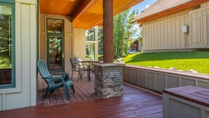 A covered outdoor deck with a stone pillar, wooden chairs, and a table.