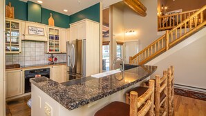 A kitchen with a granite countertop, wooden bar stools, a stainless steel refrigerator, and a sign that reads "this is your happy place."