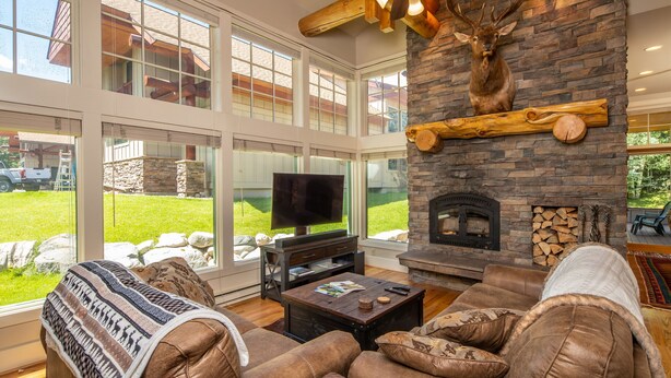A modern living room with a stone fireplace, leather sofa, and a mounted deer head.